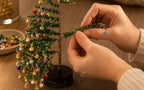 Hands attaching a beaded branch to the stand while assembling the Fleva beaded Christmas tree