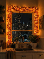 Light-up autumn leaf garland glowing around a kitchen window at night