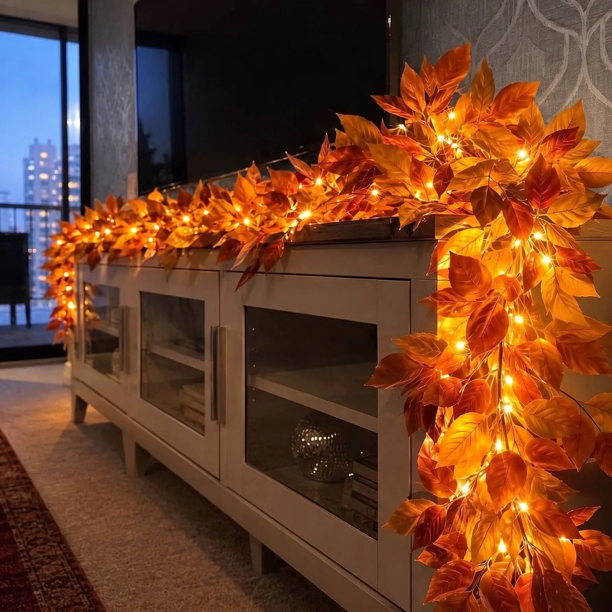 Close-up of the autumn leaf garland and its warm fairy lights on a TV console